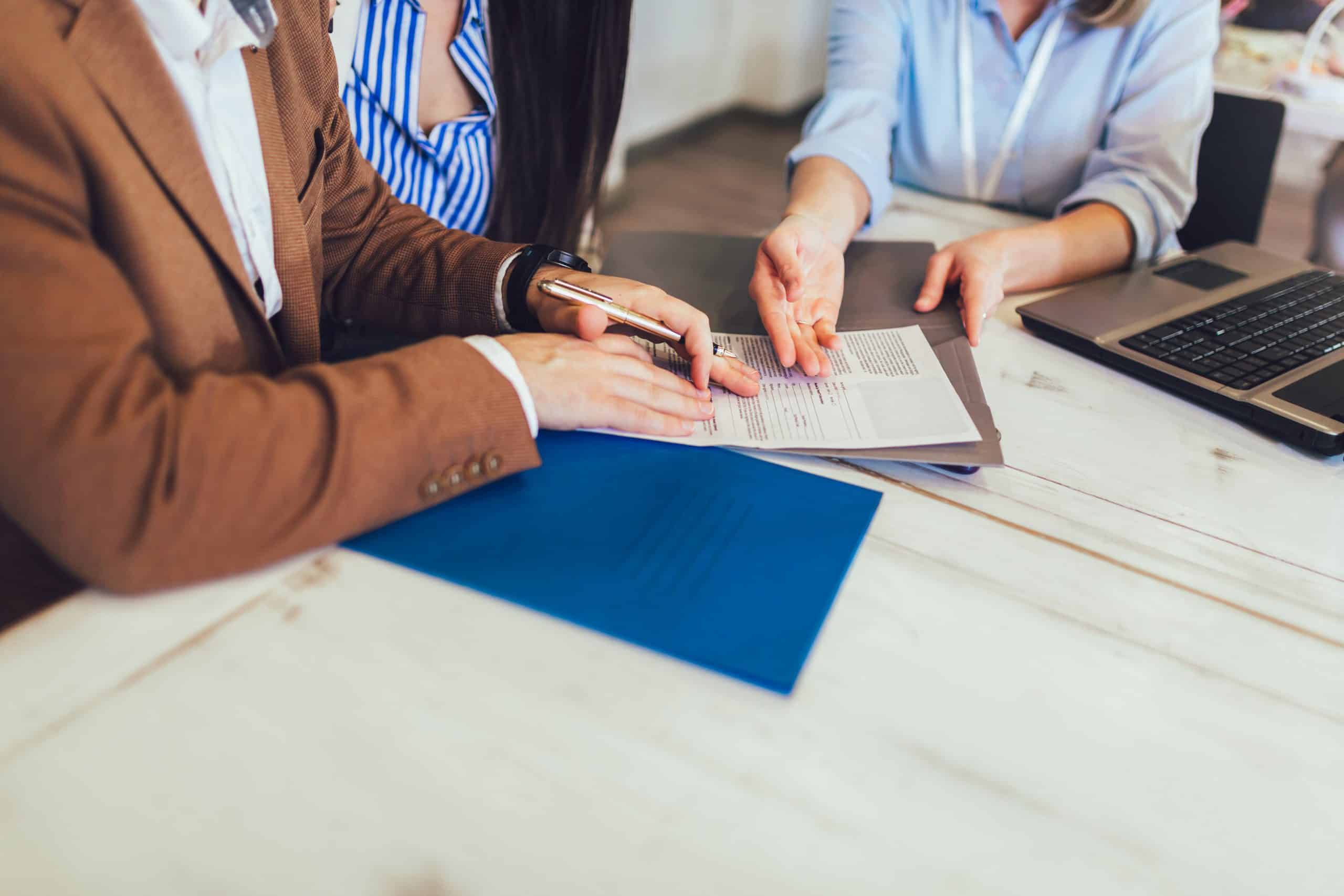 Kolme henkilöä pöydän äärellä allekirjoittamassa asiakirjaa